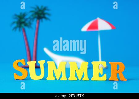 Word SUMMER aus lebendigen Holzbuchstaben mit Spielzeugpalmen, Sonnenliege und Sonnenschirm auf dem Hintergrund. Kreatives Konzept für Strandurlaub. Stockfoto