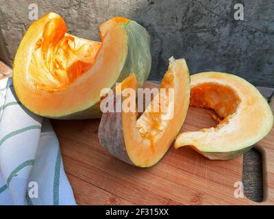 Reifer Kürbis zum Backen auf einem Holzschneidebrett in Scheiben geschnitten, Betonhintergrund, Herbststimmung, Halloween Stockfoto