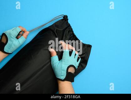 Weibliche Hände in Handschuhen halten eine Tasche mit einem verdrehten Sportmatte auf blauem Hintergrund Stockfoto