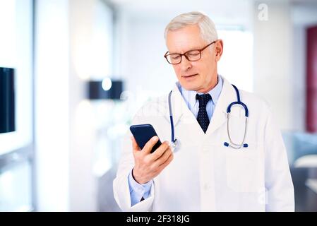 Shot von männlichen Arzt Textnachrichten, während im Zimmer des Arztes stehen. Stockfoto