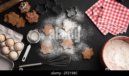 Gebackene sternförmige Lebkuchenkekse mit Puderzucker bestreut auf einem Schwarzer Tisch und Zutaten Stockfoto