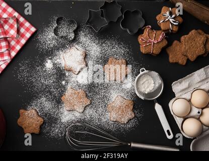 Gebackene sternförmige Lebkuchenkekse mit Puderzucker bestreut auf einem Schwarzer Tisch und Zutaten Stockfoto