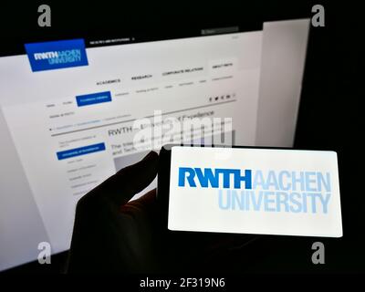 Person, die Mobiltelefon mit Logo der Rheinisch-Westfälischen Technischen Hochschule Aachen auf dem Bildschirm vor der Webseite hält. Konzentrieren Sie sich auf die Telefonanzeige. Stockfoto