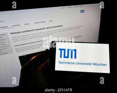 Person, die Smartphone mit Logo der Technischen Universität München auf dem Bildschirm vor der Website hält. Konzentrieren Sie sich auf die Telefonanzeige. Stockfoto