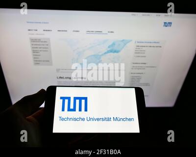 Person, die Mobiltelefon mit Logo der deutschen Bildungseinrichtung TU München auf dem Bildschirm vor der Webseite hält. Konzentrieren Sie sich auf die Anzeige von Mobiltelefonen. Stockfoto