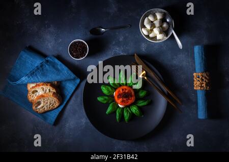 Variation von Caprese Salat, Scheiben von frischen reifen Tomaten, Mini Mozzarella, Blätter von frischem Basilikum und balsamischem Kaviar. Tabelle mit dunklem Hintergrund. Stockfoto