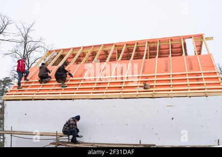 Irpin - Ukraine, März - 13, 2021: Dachdecker Installation von Dachplatten und Dampfsperren für Metallfliesen im Winter. Isolierung des Fac Stockfoto