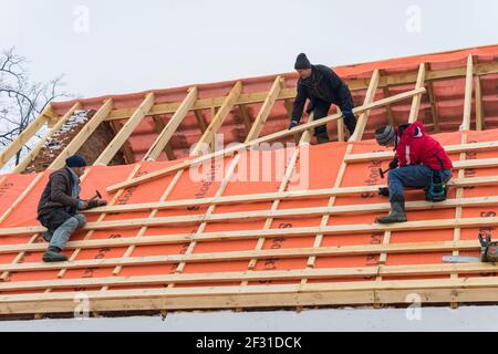 Irpin - Ukraine, März - 13, 2021: Dachdecker Installation von Dachplatten und Dampfsperren für Metallfliesen im Winter. Stockfoto