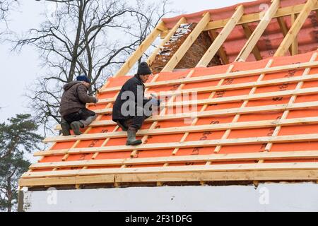 Irpin - Ukraine, März - 13, 2021: Dachdecker Installation von Dachplatten und Dampfsperren für Metallfliesen im Winter. Stockfoto
