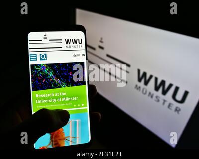 Person, die Mobiltelefon mit Webseite der Bildungseinrichtung Universität Münster auf dem Bildschirm vor dem Logo hält. Konzentrieren Sie sich auf die Mitte des Telefondisplays. Stockfoto