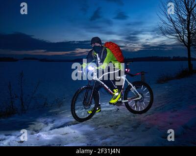 Guy Radfahrer sitzt auf einem MTB während einer Nachtfahrt. Stadtpark und leichter Schneefall im Nebel. Stockfoto