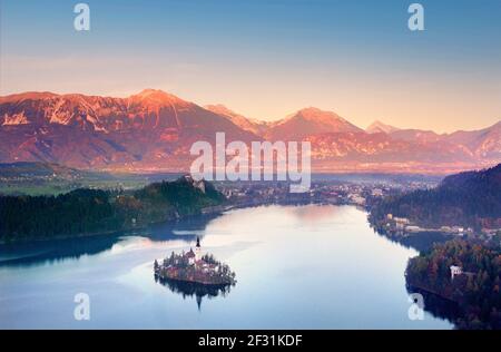 INSEL BLED SEE KIRCHE SLOWENIEN Hochansicht See vista Landschaft Die Insel und die Kirche auf einem perfekten stillen See Bled Bei rotem Sonnenuntergang mit Herbstfarbe Julische Alpen mit Kulisse Sonne hinter Slowenien Stockfoto