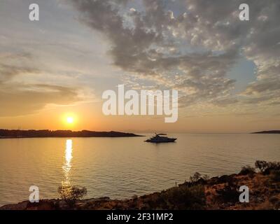 Orangefarbene Sonnenuntergangssonne über griechischen Inseln in der Ägäis in Griechenland. Sommer Tourismus Reisen. Malerische Wolken und Yacht in ruhigen Meer am Abend Stockfoto