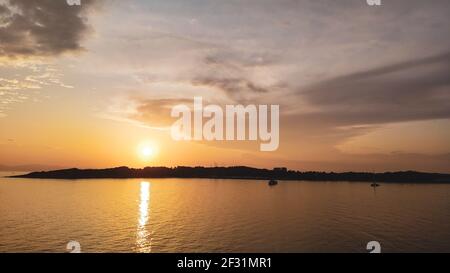 Orangefarbene Sonnenuntergangssonne über griechischen Inseln in der Ägäis bei Athen in Griechenland. Sommer Tourismus Reisen. Malerische Wolken und Yachten in ruhigen Meer in even Stockfoto