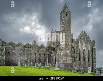 Friedhof mit keltischen Kreuzen und Grabsteinen vor der majestätischen Burg Rock of Cashel, Grafschaft Tipperary, Irland Stockfoto