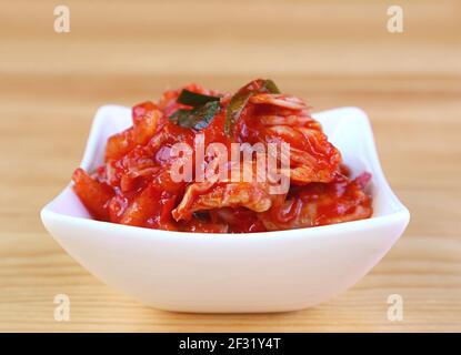 Nahaufnahme von Kimchi, einem ikonischen koreanischen Gericht in White Bowl auf Holzhintergrund Stockfoto