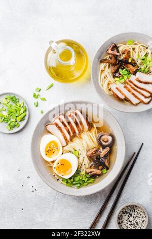 Asiatische Nudelsuppe Ramen mit Huhn und Shiitake Pilze auf grauem Beton Hintergrund, Tabelle Draufsicht. Zwei Schalen von Ramen Stockfoto