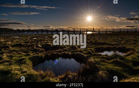 East Lothian, Schottland, Großbritannien, 14th. März 2021. UK Wetter: Sonnenuntergang im Aberlady Naturreservat. Die Sonne geht über das Feuchtgebiet in Aberlady Bay und die hölzerne Fußgängerbrücke unter Stockfoto