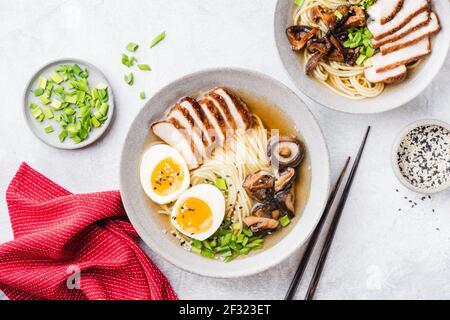 Chicken Shiitake Ramen Nudelsuppe Schüssel auf einem grauen Beton Hintergrund, Draufsicht. Asiatische Küche, Nudelsuppe mit Huhn, Shiitake, Ei und Grün Stockfoto