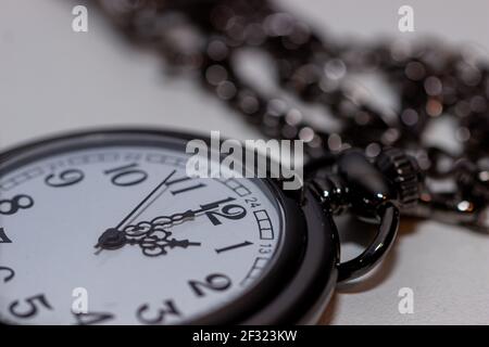 Nahaufnahme einer schwarzen Vintage-Taschenuhr auf weißer Oberfläche. Stockfoto