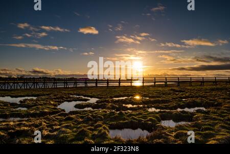 East Lothian, Schottland, Großbritannien, 14th. März 2021. UK Wetter: Sonnenuntergang im Aberlady Naturreservat. Die Sonne geht über das Feuchtgebiet in Aberlady Bay und die hölzerne Fußgängerbrücke unter Stockfoto
