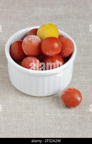 Gefrorenes Gemüse - Tomaten Kirsche - in Schüssel auf Leinentuch Hintergrund, Nahaufnahme, sparen Reste, Lebensmittelaufbewahrung Konzept und Essen von Mahlzeiten zu Hause con Stockfoto