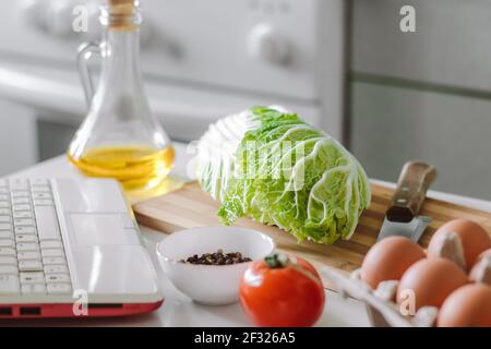 Online-Kochen. Salat mit digitalem Kochbuch zubereiten. Frisches Gemüse und Laptop in der heimischen Küche. Stockfoto