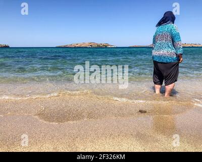 Muslimische Frau, die auf dem Sandstrand läuft, während ihre Füße Im Sommer mit ihren Kleidern im Meer Stockfoto