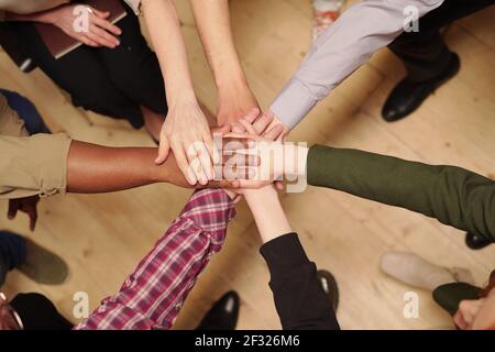 Überblick über mehrere interkulturelle Patienten der zeitgenössischen psychologischen Gruppengestaltung Stapel von Händen während der Sitzung, während sie im Kreis sitzen Stockfoto