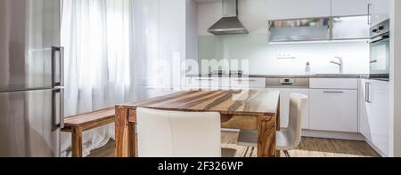 Moderne Küche Interior Design Architektur Stock Image, Foto von einer modernen weißen Küche mit einem dunklen Holztisch, High-End-Geräte und viel Tageslicht Stockfoto