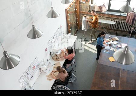 Gruppe von jungen zeitgenössischen Modedesignern und Schneidern tun individuelle Arbeit über neue saisonale Kollektion in Workshop Stockfoto