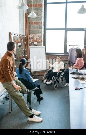 Junge kreative Designerin im Rollstuhl, die auf Skizze zeigt Whiteboard während der Präsentation auf Seminar in Workshop Stockfoto