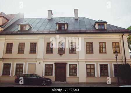 Beigefarbenes Haus mit braunen Fenstern, Holztür, grauem Dach und Auto davor Stockfoto