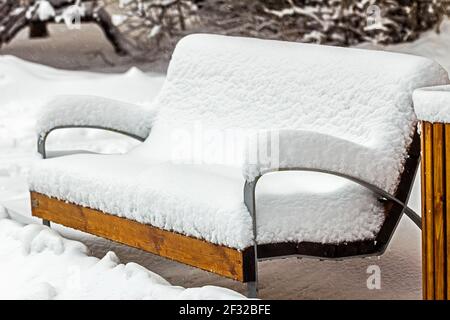 Echte hübsche Holzbank, die tagsüber komplett mit Schnee bedeckt ist Stockfoto