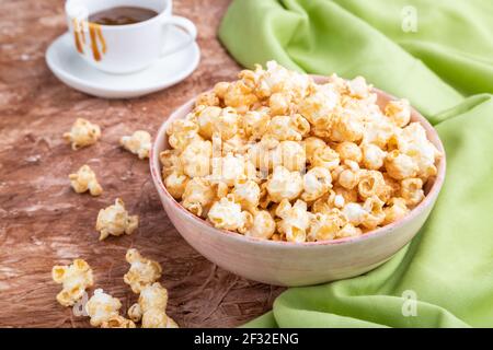 Popcorn mit Karamell in Keramikschale auf braunem Betongrund und grünem Textil. Seitenansicht, Nahaufnahme. Stockfoto