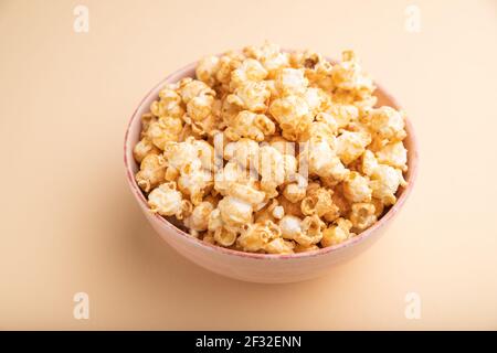 Popcorn mit Karamell in Keramik-Schüssel auf pastellorangefarbenem Hintergrund. Seitenansicht, Nahaufnahme. Stockfoto
