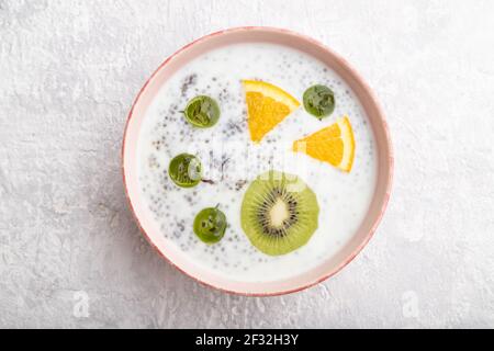 Joghurt mit Kiwi, Stachelbeere, Chia in Keramikschale auf grauem Betongrund. Draufsicht, Nahaufnahme. Stockfoto