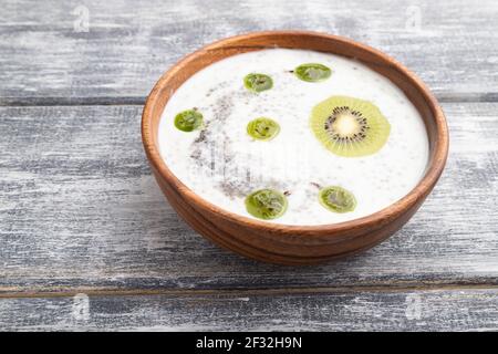 Joghurt mit Kiwi, Stachelbeere, Chia und Mandeln in Holzschüssel auf grauem Holzhintergrund. Seitenansicht, Nahaufnahme. Stockfoto