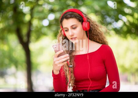 Rot gekleideter Teenager, der in einem Park Musik vom Telefon hört Stockfoto