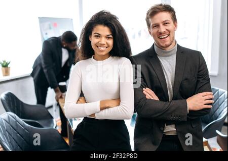 Portrait von jungen erwachsenen Geschäftspartnern stehen mit Kreuzhände in modernen Büro,. Glückliche selbstbewusste multiethnische Kollegen in formeller Kleidung Blick auf die Kamera, lächelnd, Teamwork-Konzept Stockfoto