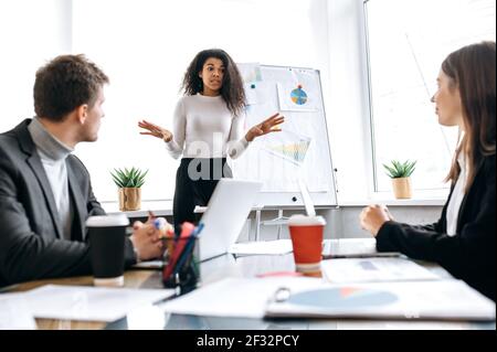 Serious weibliche Chef des Unternehmens eine Präsentation über den Unternehmensgewinn für die Mitarbeiter. Stilvolle einflussreiche junge Geschäftsfrau spricht über Finanzberichte auf Briefing Meeting, Konferenzkonzept Stockfoto