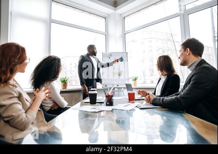 afroamerikanische zuversichtlich Geschäftsmann, die Präsentation auf Konferenz, reden über Finanzgraphen. Stilvoller männlicher Mitarbeiter legt Arbeitsbericht zum Briefing-Meeting vor Stockfoto