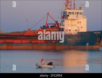 Ein Bagger, der mit Vater und Tochter an einem kleinen Beiboot vorbeifährt. Shoreham Harbour, Sussex, England, Großbritannien Stockfoto