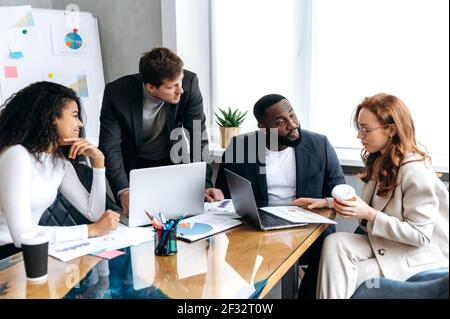 Fokussierte Geschäftsleute auf Konferenz im Büro, Schreibarbeit, Projektdiskussion. Erfolgreiche junge Erwachsene Mitarbeiter lernen Finanzgraphen, machen einen Bericht, arbeiten zusammen Stockfoto