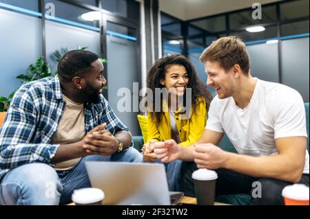 Fröhliche, freundliche Kollegen oder Studenten, die im modernen Büro sitzen und ein angenehmes Gespräch führen. Multiethnische Mitarbeiter sprechen über Projekt, diskutieren Ideen, Teamwork-Konzept Stockfoto