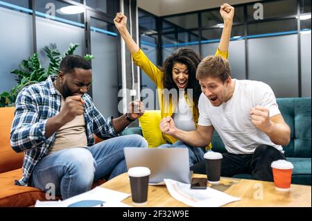 Überglücklich fühlen sich Mitarbeiter oder Studenten im Büro euphorisch, blicken auf den Laptop-Bildschirm und schreien. Aufgeregt männlich und weiblich Bestehen wichtige Prüfungen oder einen großen Gewinn aus Unternehmensprojekt Stockfoto