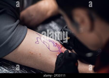 Nahaufnahme eines Mädchens Tattoo-Künstlers, der ein Tattoo auf den Arm eines jungen Mannes in einem Tattoo-Salon mit der Handpoke-Methode setzt. Stockfoto