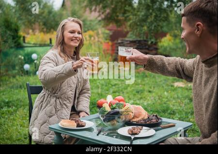 Ein junges Paar feiert einen Familienurlaub, Dating und Hochzeitstag. Ein Mann und eine Frau klirken Gläser Bier, während sie an einem Tisch sitzen Stockfoto