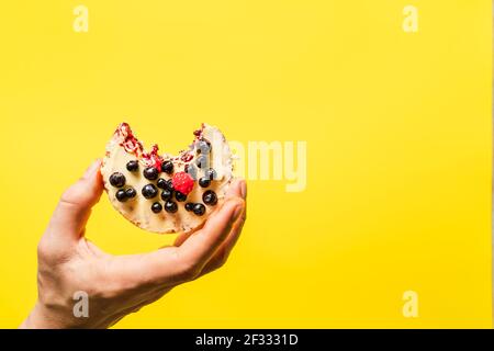 Hand halten knusprig aufgeblasen Reiskuchen mit frischen Früchten Blaubeeren Himbeeren vor dem gelben Hintergrund - gesund Bio-Vegetarier oder ve Stockfoto