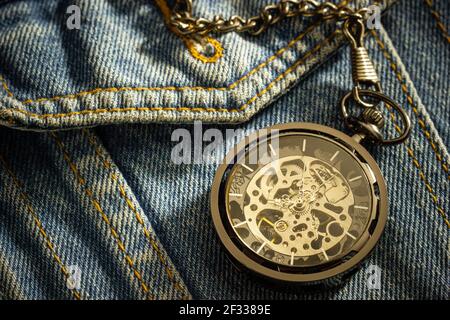 Vintage Taschenuhr ist über einem alten blauen Denim-Shirt platziert und die Morgensonne scheint in der oberen rechten Ecke. Das Konzept der Zeitbedeutung. C Stockfoto